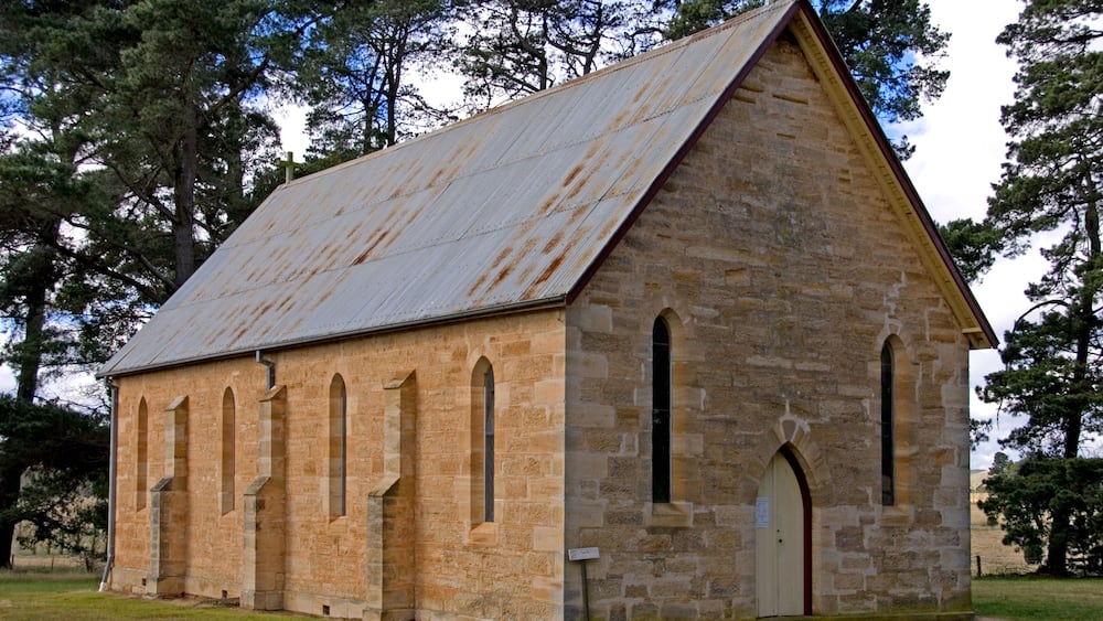 A stone church with a metal roof and arched windows.