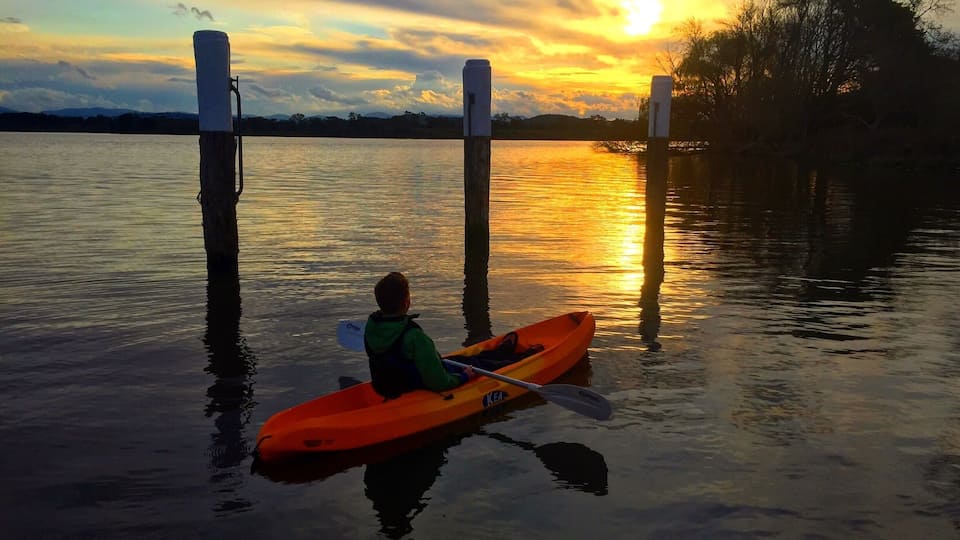Eine Person sitzt in einem Kajak auf einem ruhigen See bei Sonnenuntergang.