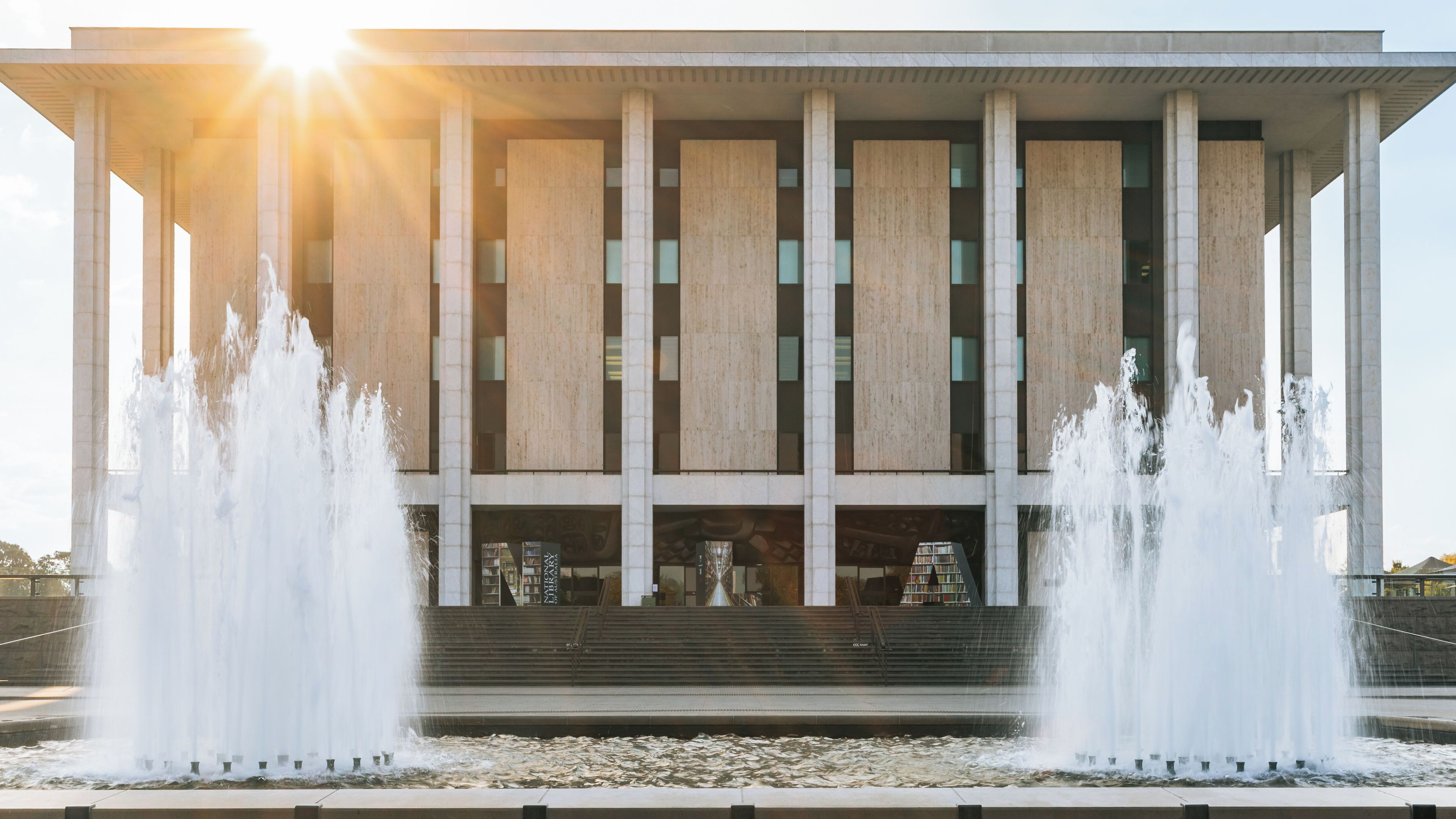 A modern building with a series of vertical columns and a water fountain in front.