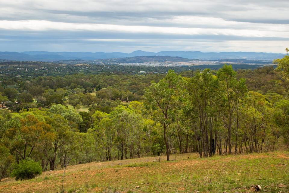 Un paisaje montañoso con densos bosques verdes, un pueblo distante y montañas al fondo.