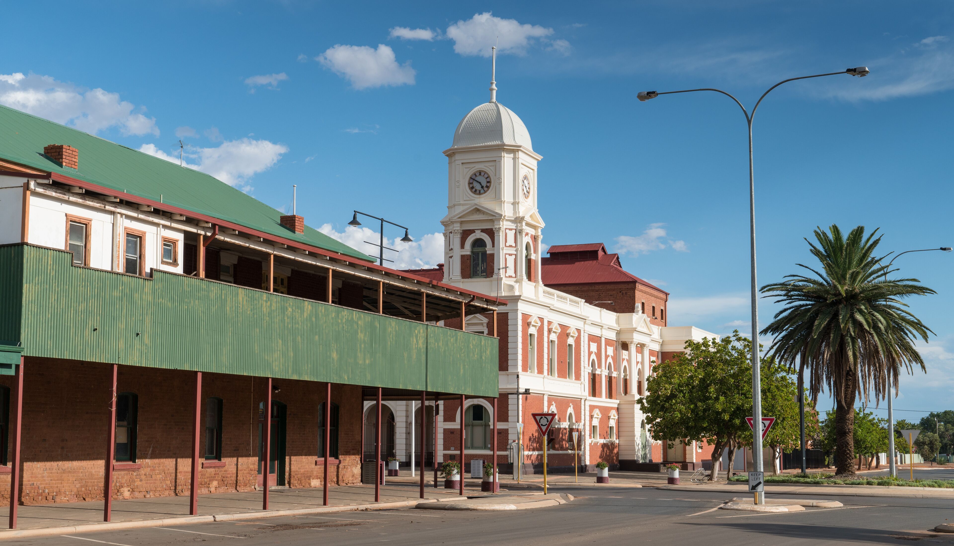 A historic building with a clock tower, a green-roofed structure, and palm trees.