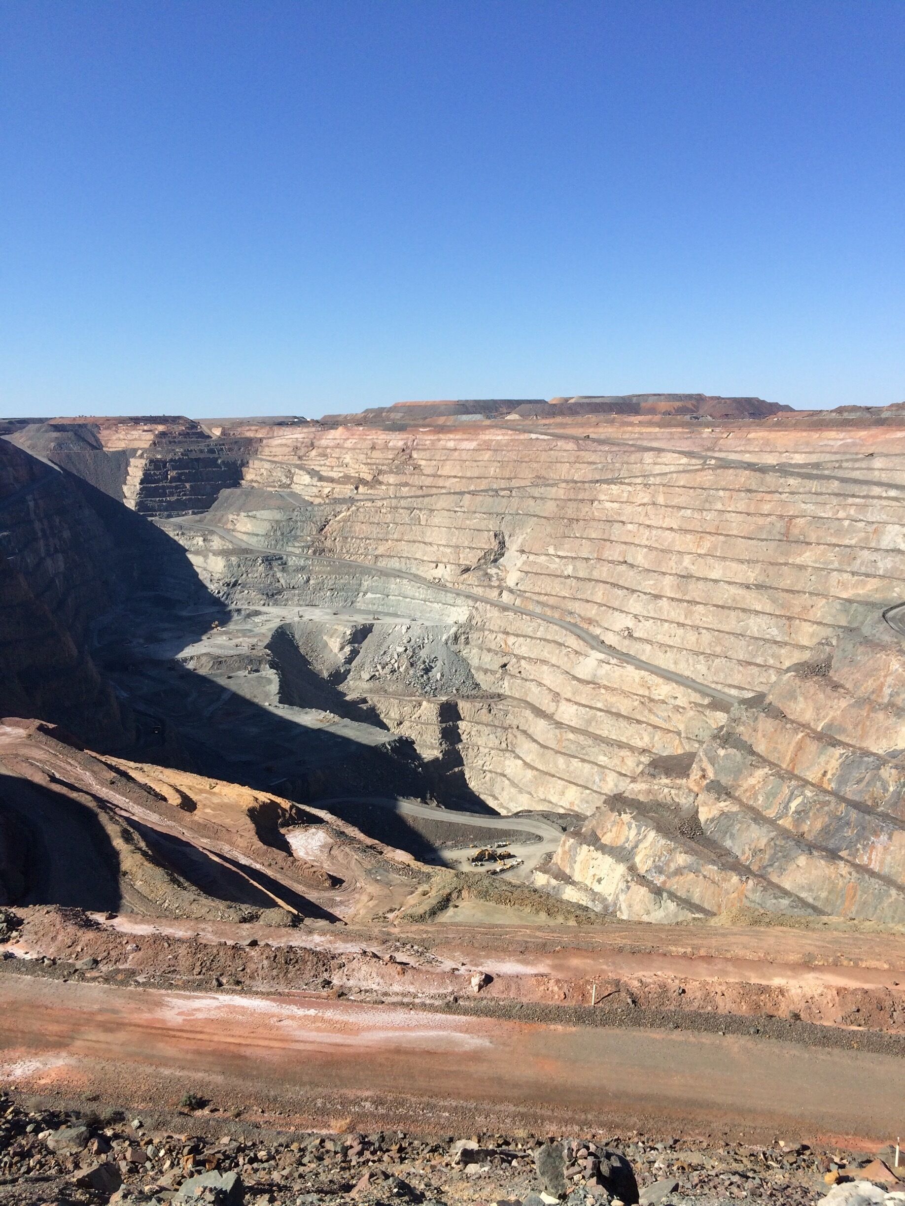 A vast open-pit mine with layered earth and a clear blue sky.