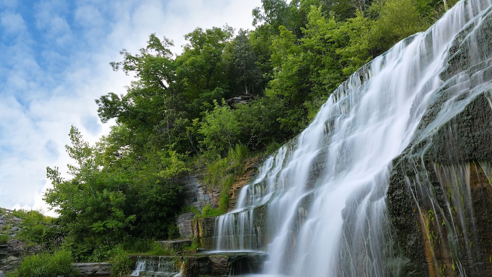 A multi-tiered waterfall surrounded by lush green forest.