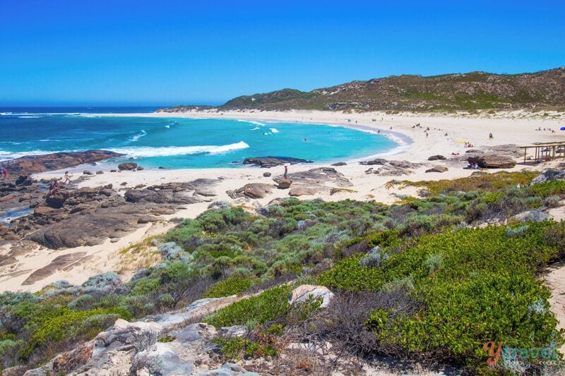 A coastal landscape with a sandy beach, rocky outcrops, and green vegetation.