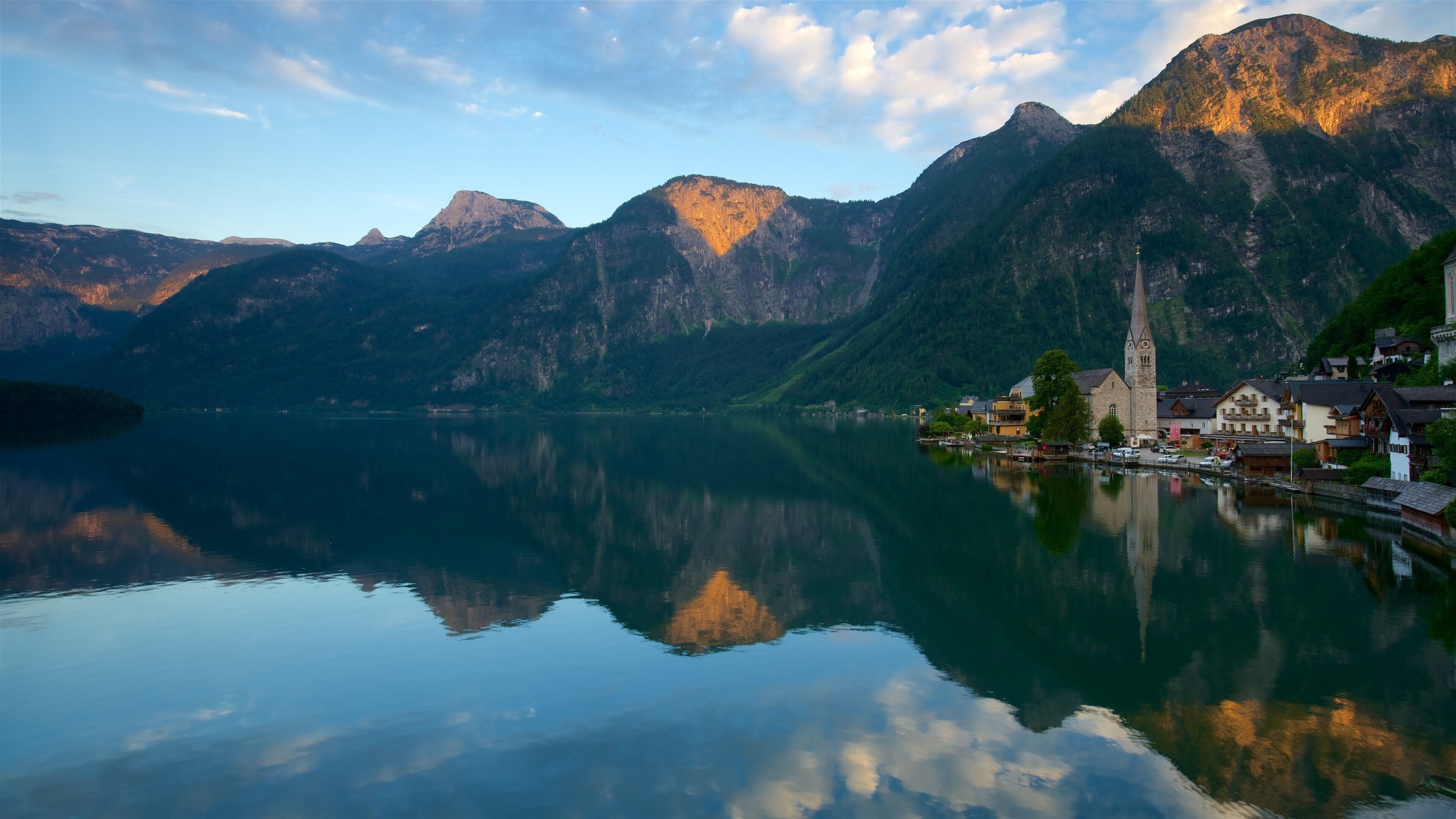 A calm lake reflecting mountains and a church with a tall steeple.
