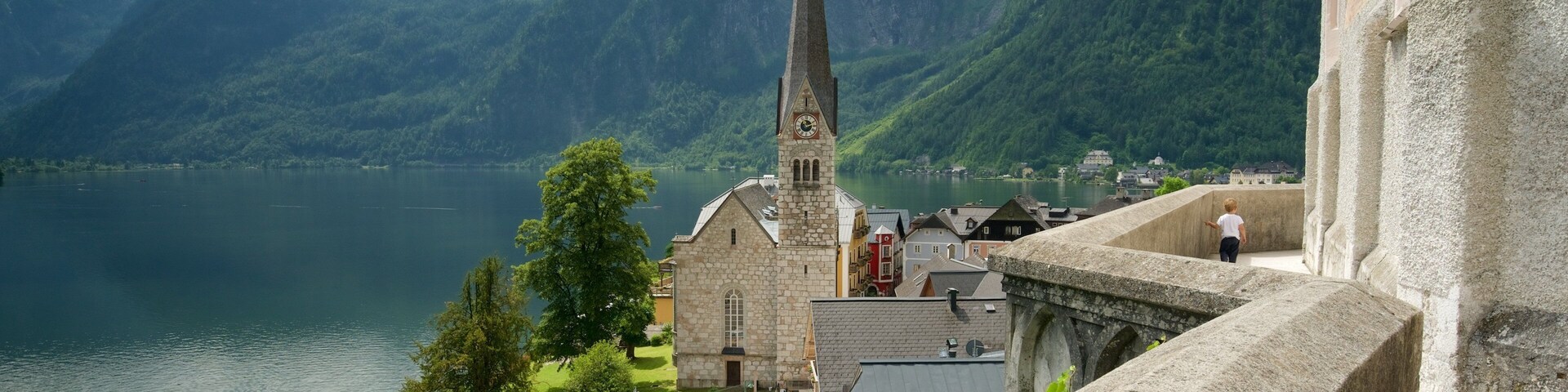 Uma igreja com uma torre alta, um corpo d'água e montanhas ao fundo.