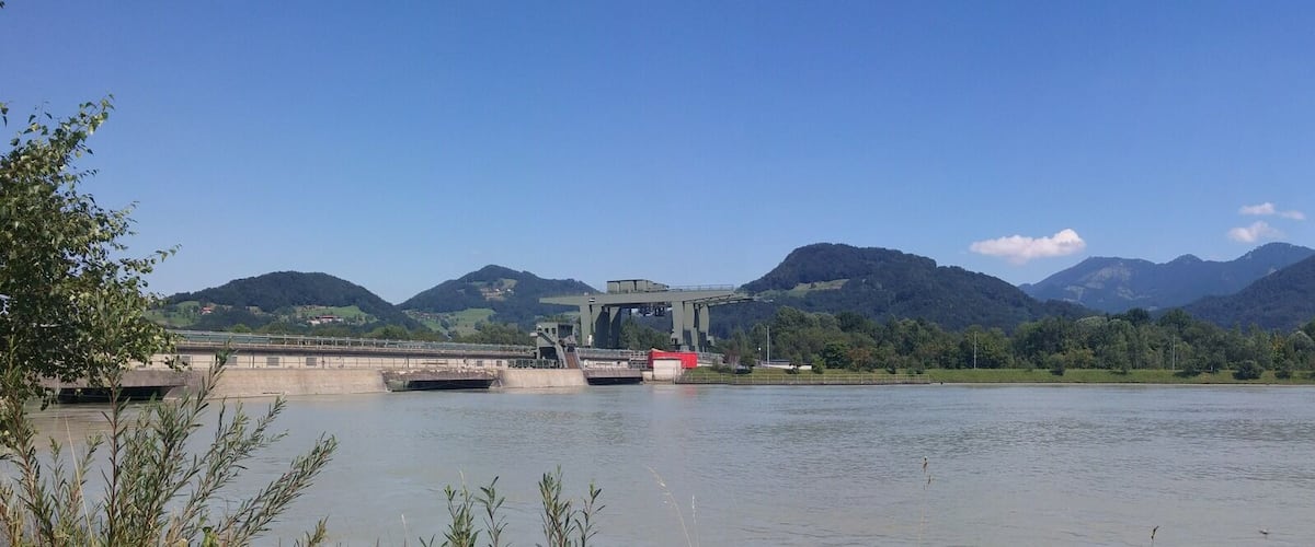 A calm lake with mountains in the background, a bridge, and a clear sky.