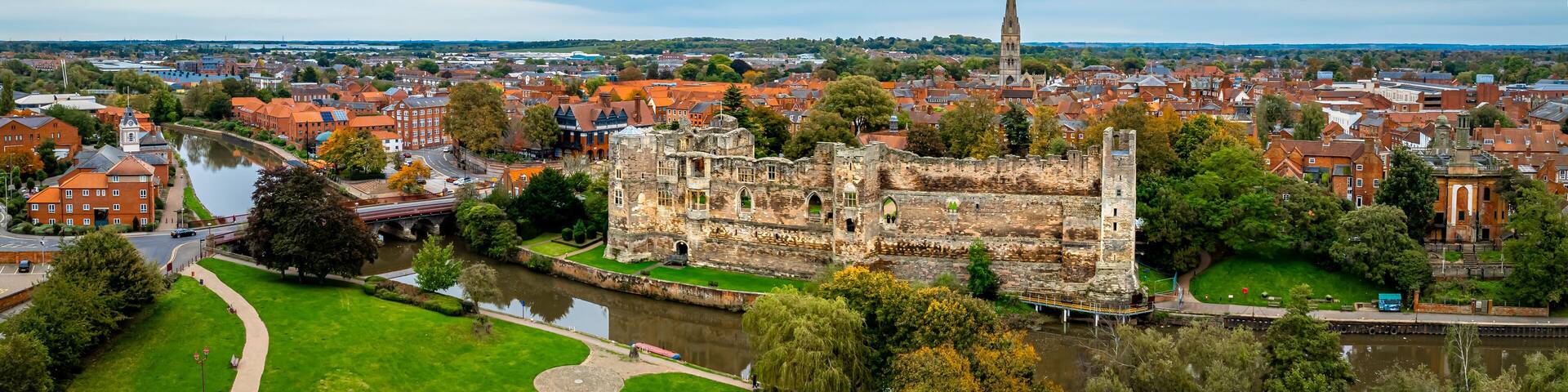A historic castle with a river, surrounded by a town with red-roofed buildings and a church spire.