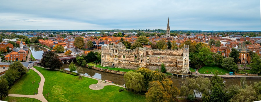 A historic castle with a river, surrounded by a town with red-roofed buildings and a church spire.