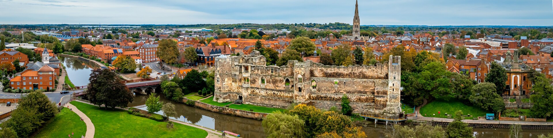 Un castillo histórico con un río, rodeado por un pueblo de edificios con tejados rojos y una aguja de iglesia.