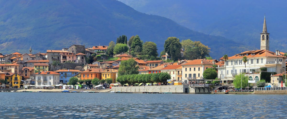 A lakeside town with colorful buildings, a church tower, and mountains in the background.