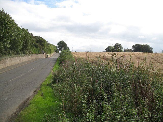 Road beside Riccarton Campus Heriot Watt University lurks behind the policy wall of Riccarton House. Arable land to the right.