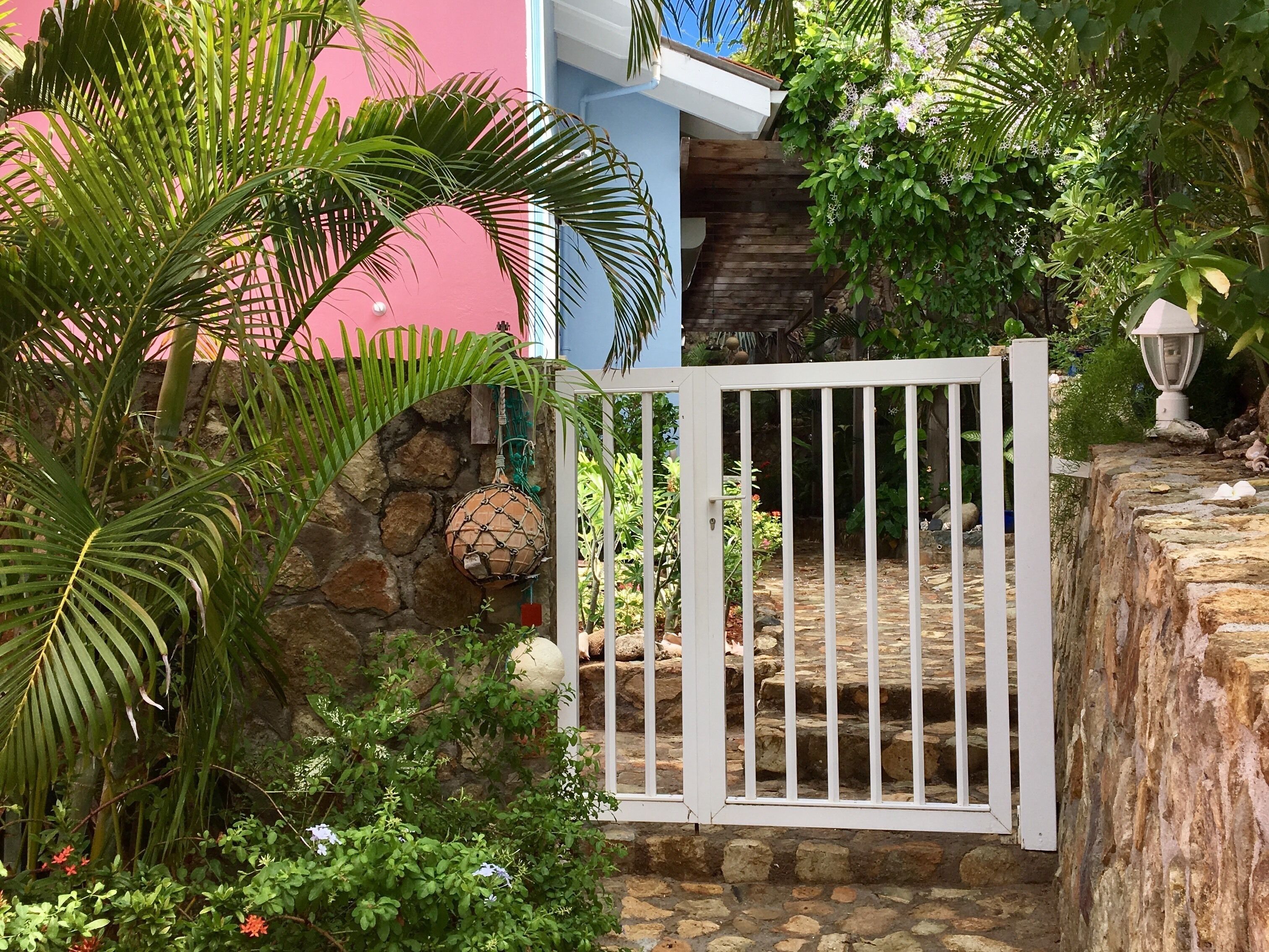 A white gate, a stone wall, and a pink building.
