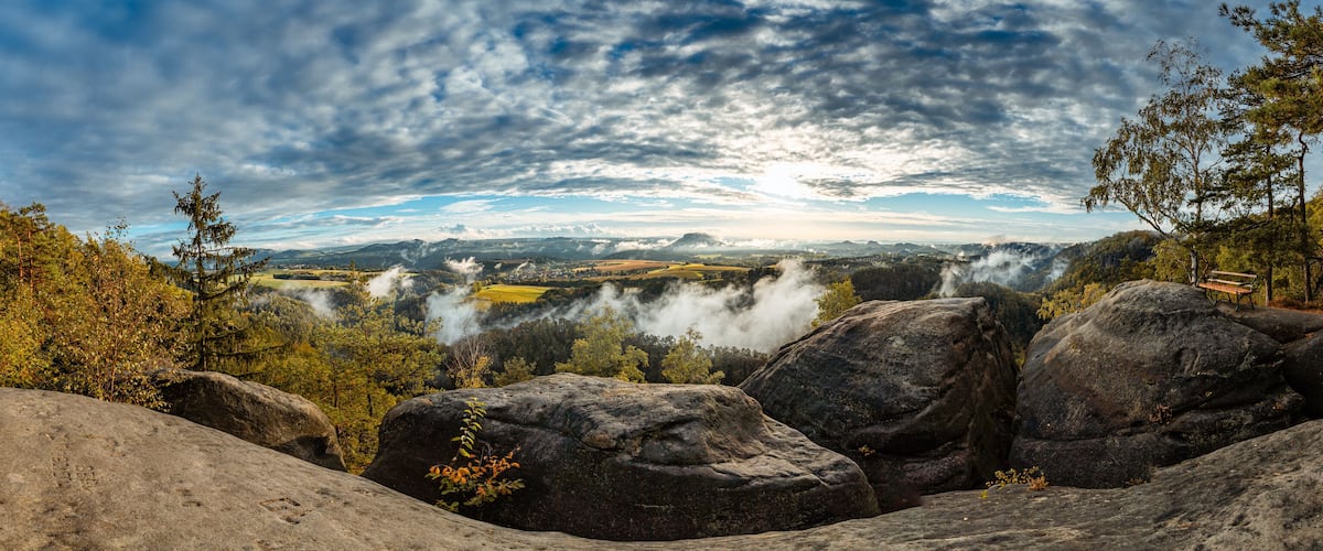 A mountainous landscape with large rocks, trees, and a bench.