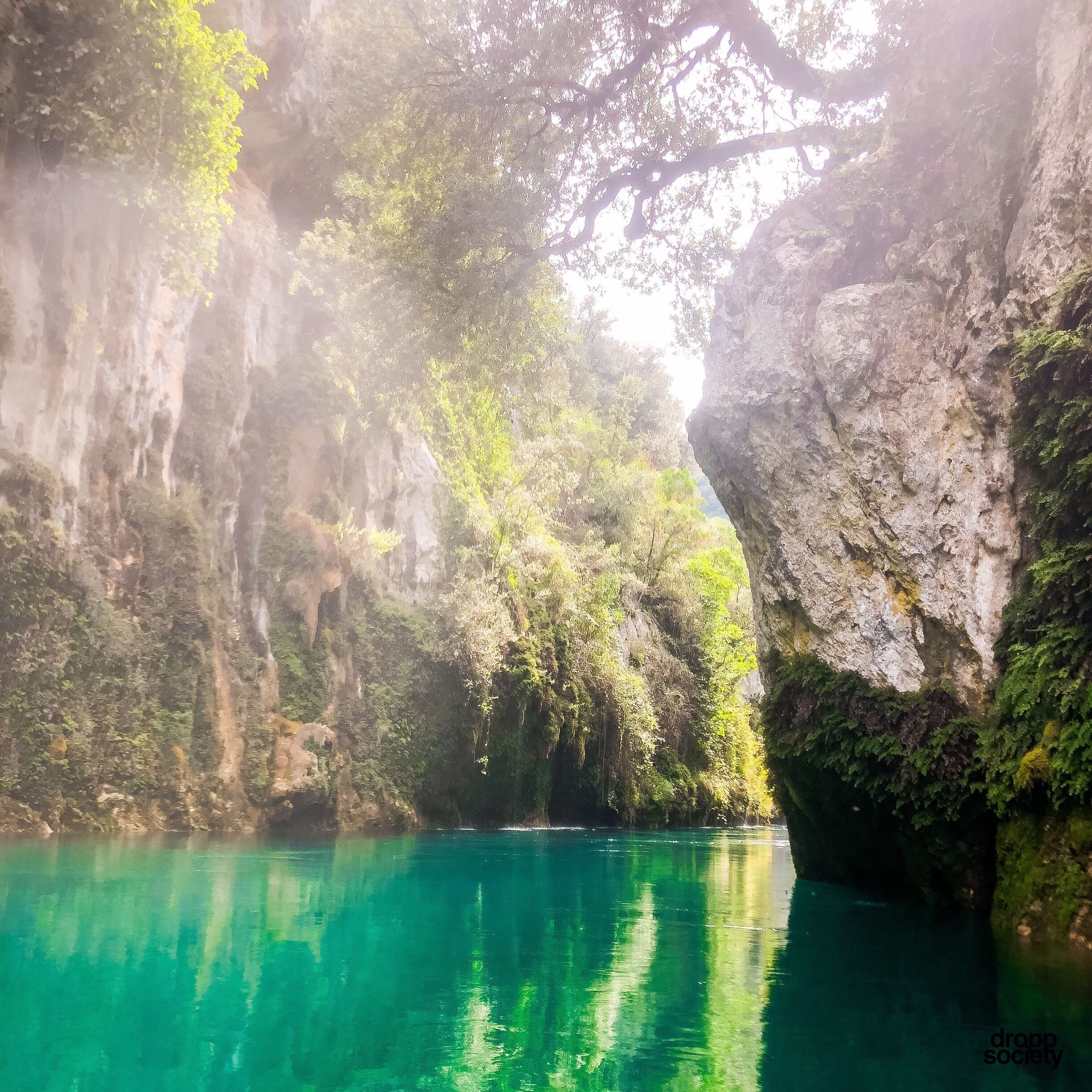 A turquoise river surrounded by lush greenery and rocky cliffs.