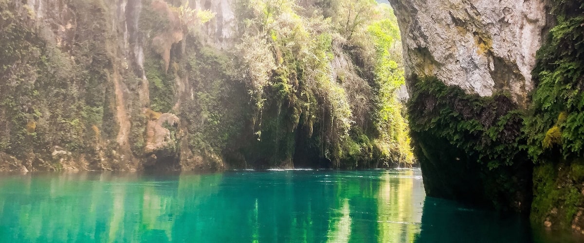 A turquoise river surrounded by lush greenery and rocky cliffs.