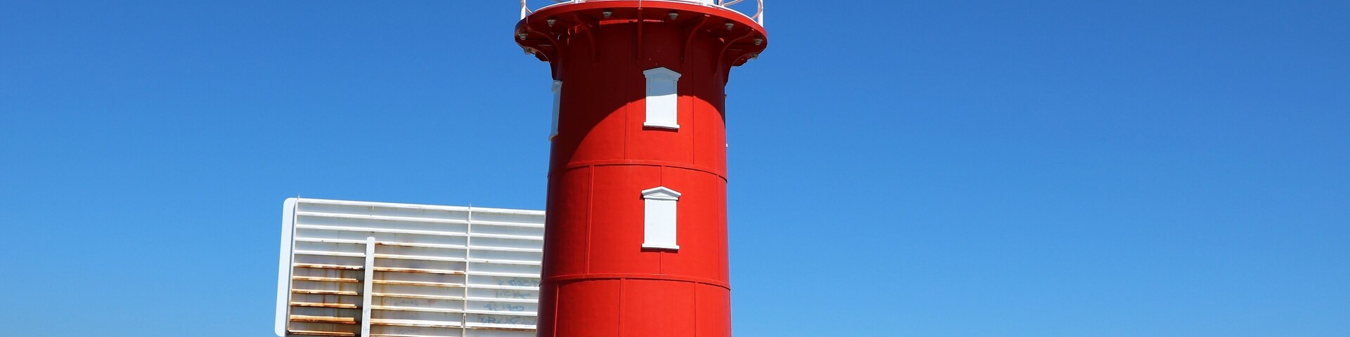 Un faro rojo con la parte superior blanca, rodeado por una valla blanca y rocas.