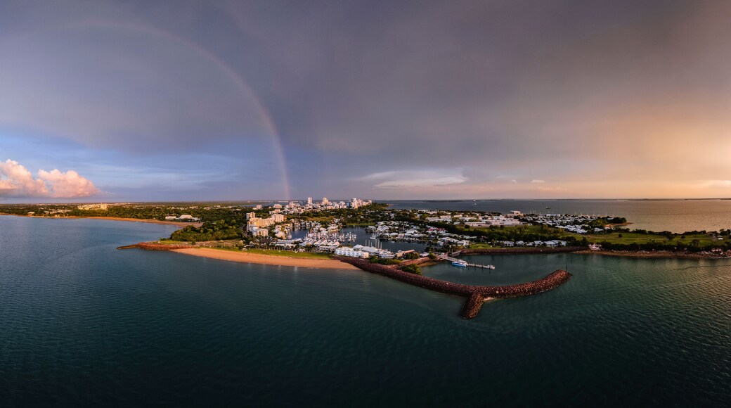 A coastal city with a marina, a lighthouse, and a rainbow over the water.