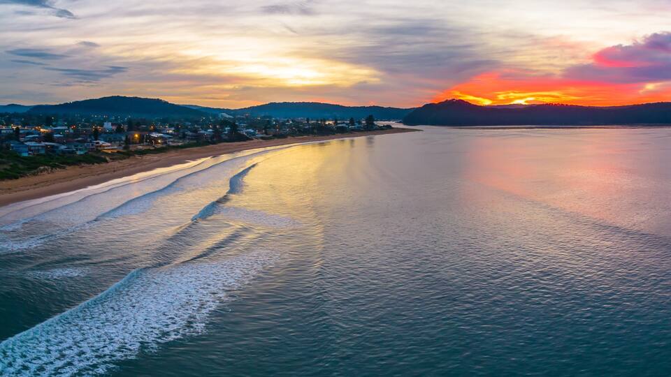 A coastal landscape with a sunset, calm sea, and a town along the shore.