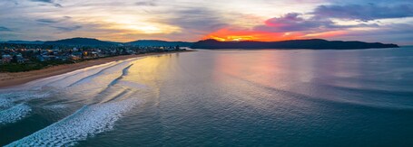 A coastal landscape with a sunset, calm sea, and a town along the shore.