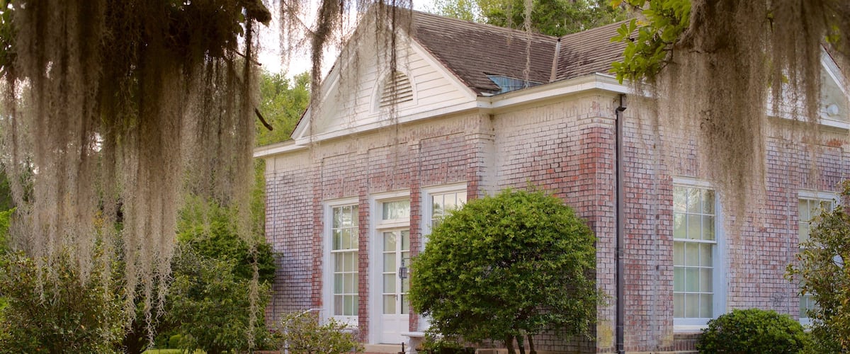 A historic brick building with white trim and a gabled roof, surrounded by mature trees and well-maintained landscaping.