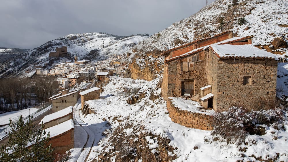 A snow-covered village with stone buildings and a church on a hillside.