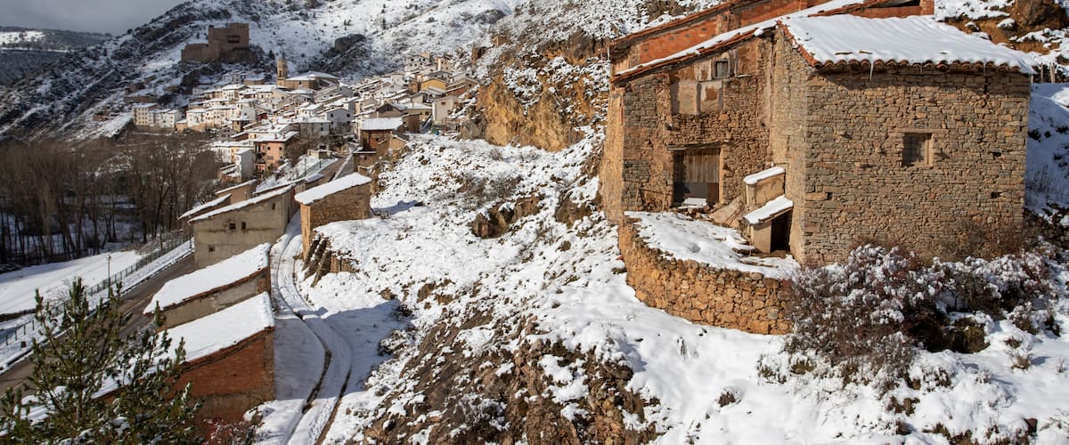 A snow-covered village with stone buildings and a church on a hillside.