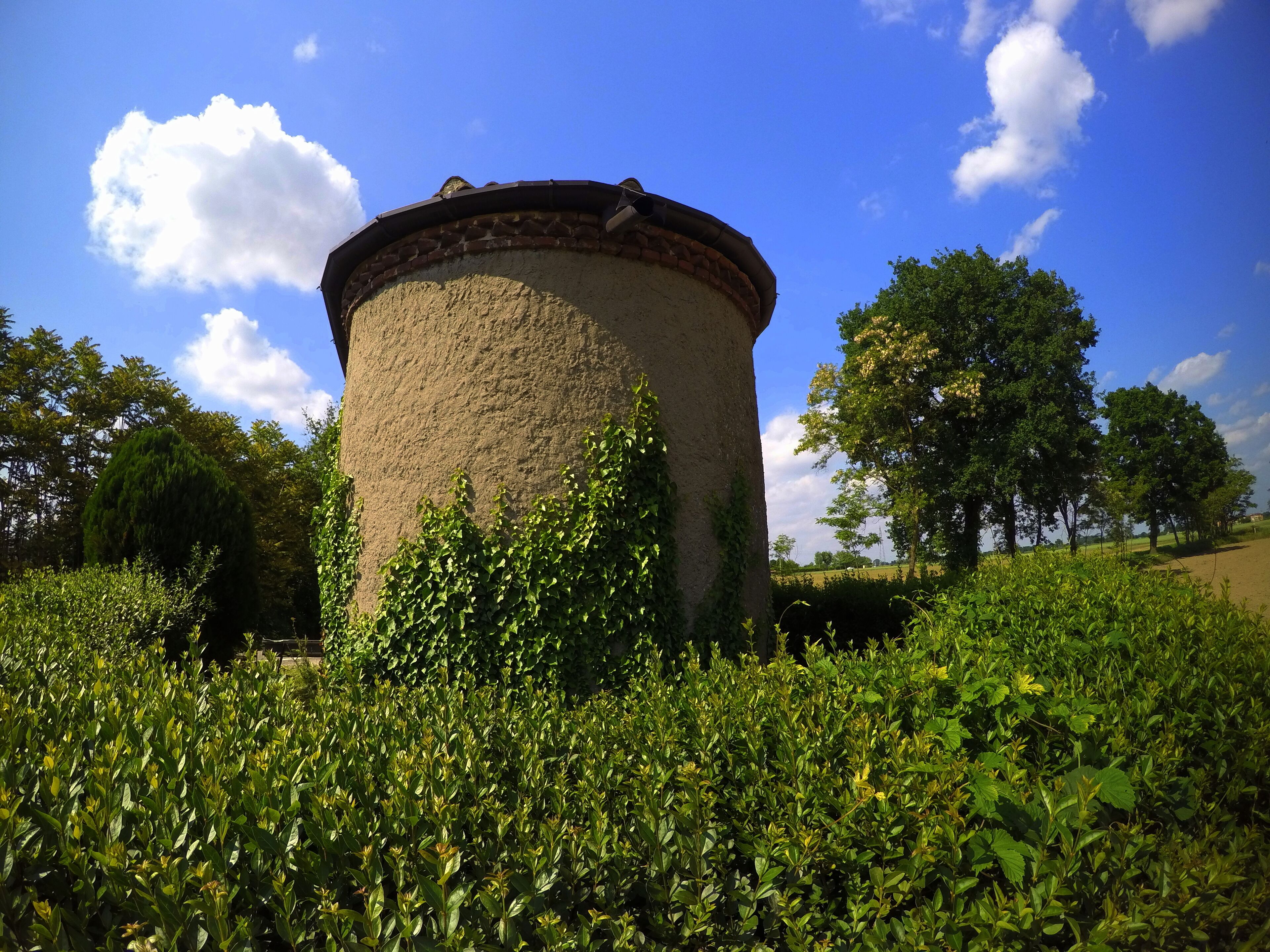 A cylindrical tower surrounded by lush greenery and trees under a clear blue sky.