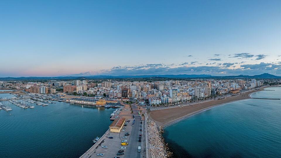 A coastal cityscape with a marina, a beach, and a mountain in the background.