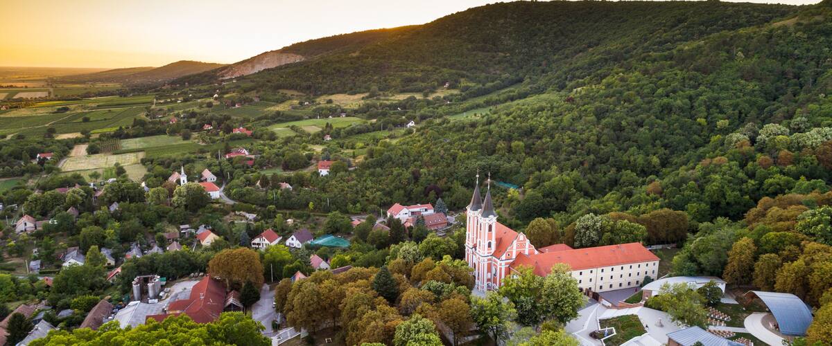 An aerial view of a town with a prominent church, rolling hills, and scattered houses.
