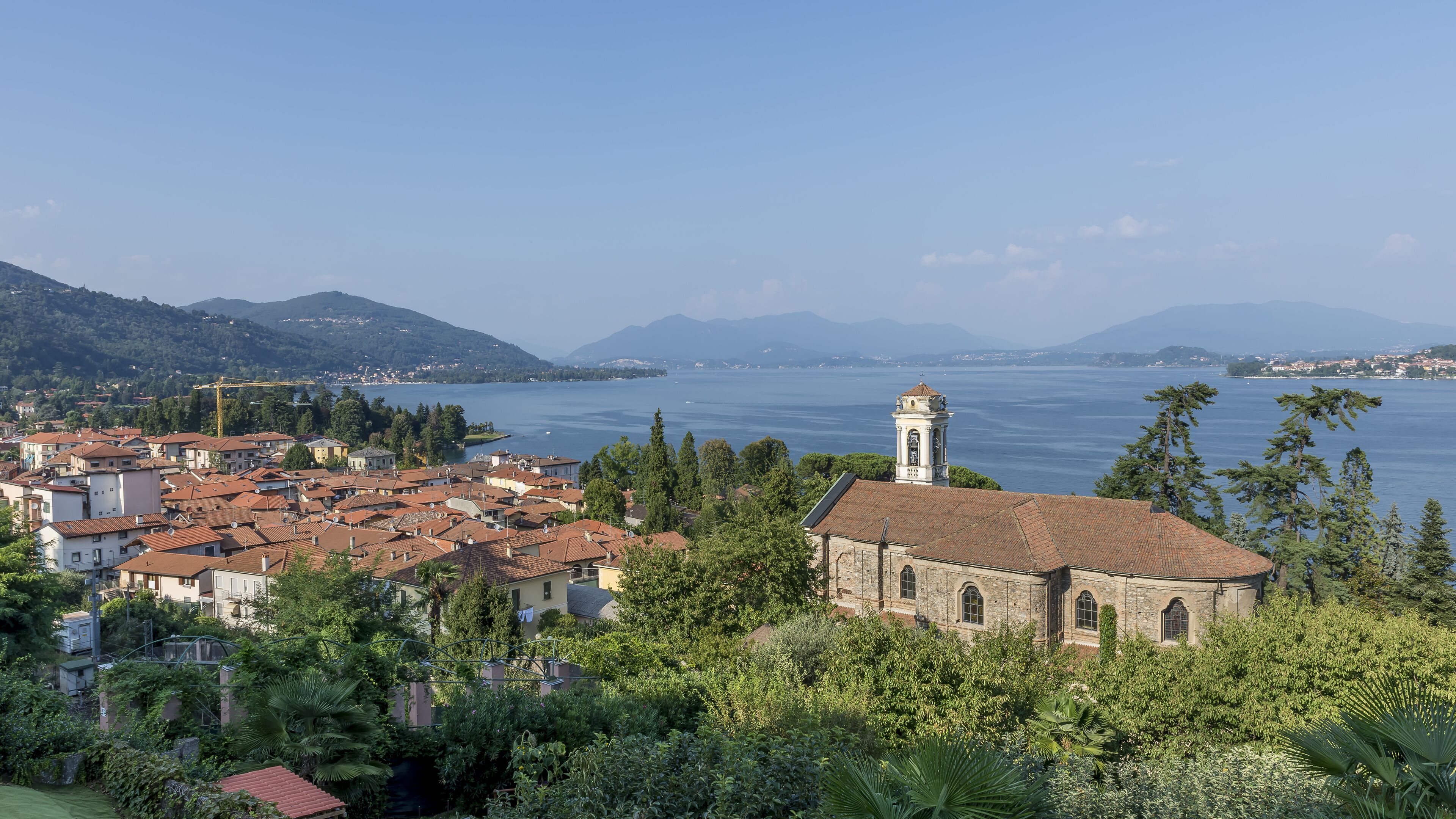A coastal town with a prominent church, lush greenery, and a clear view of the sea and distant mountains.