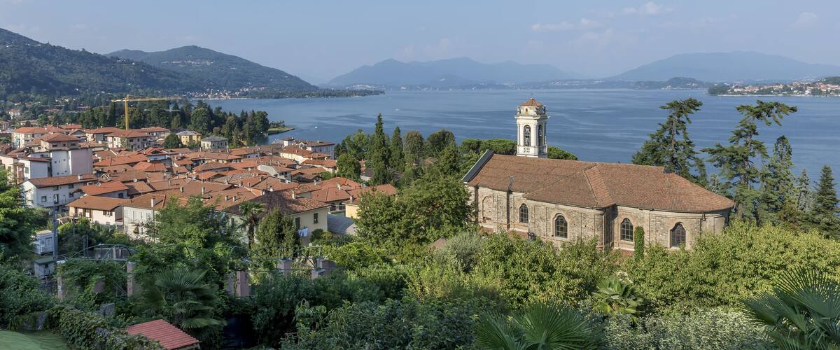 A coastal town with a prominent church, lush greenery, and a clear view of the sea and distant mountains.