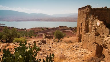 A desert landscape with a large body of water, mountains in the background, and ancient ruins.