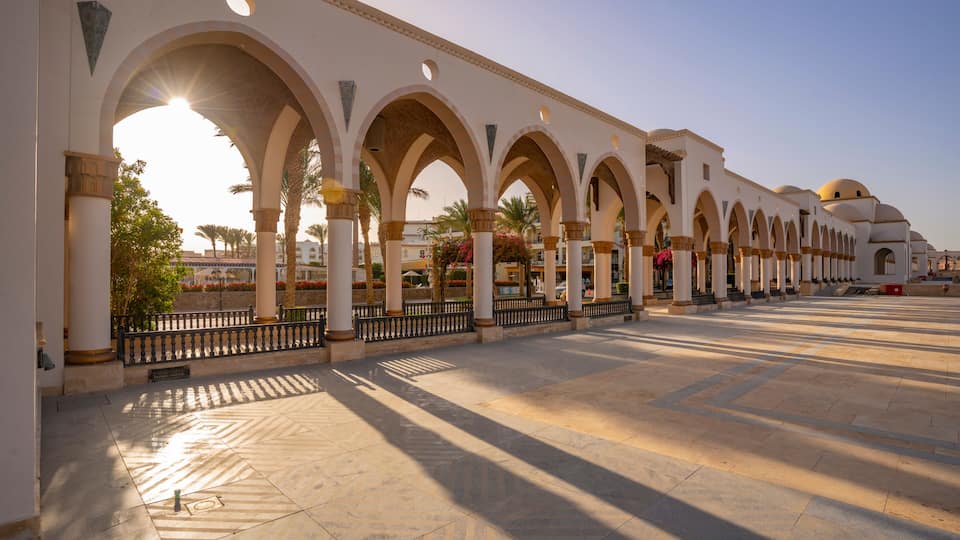 A series of arches, a paved plaza, and a building with domed roofs.