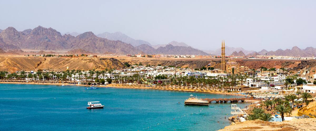 A coastal city with a prominent mosque, palm-lined beaches, and mountains in the background.