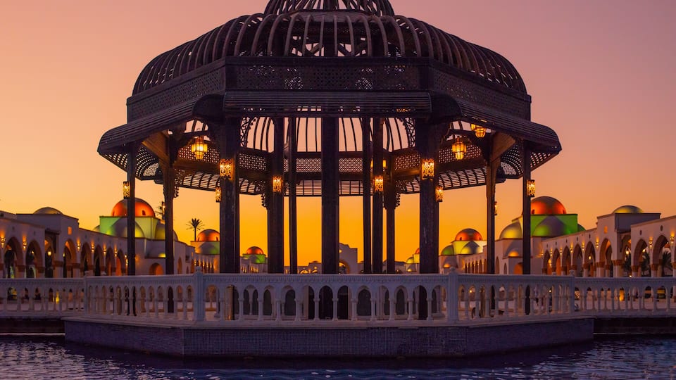 A domed pavilion with a white balustrade, set against a sunset sky.