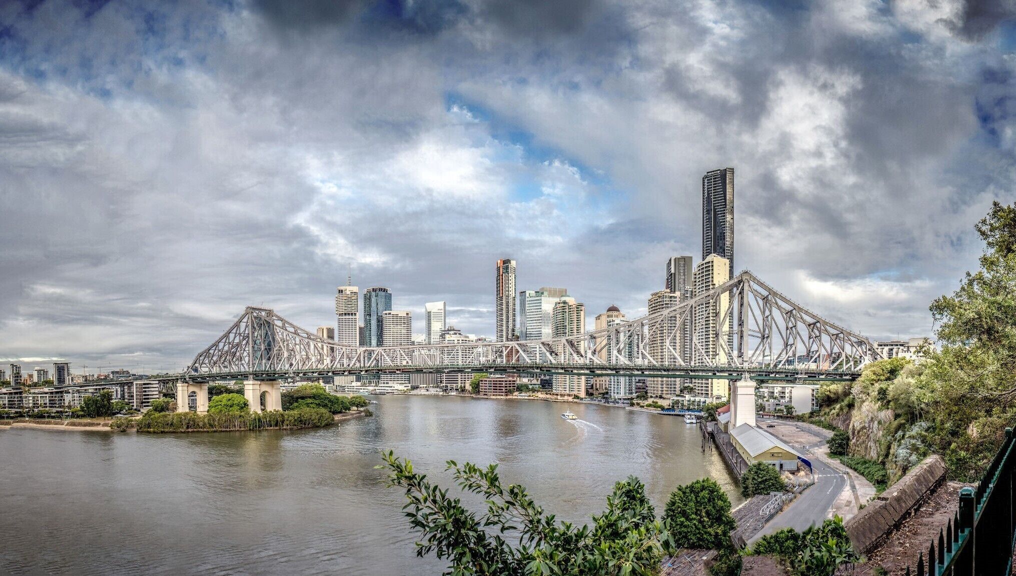 A cityscape with a prominent bridge over a river, surrounded by modern skyscrapers and lush greenery.