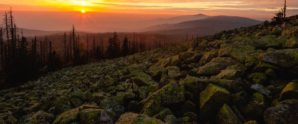 A mountainous landscape with a sunset, rocky terrain, and a forested area.