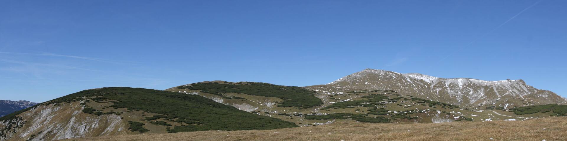 A mountain range with green vegetation and snow patches.