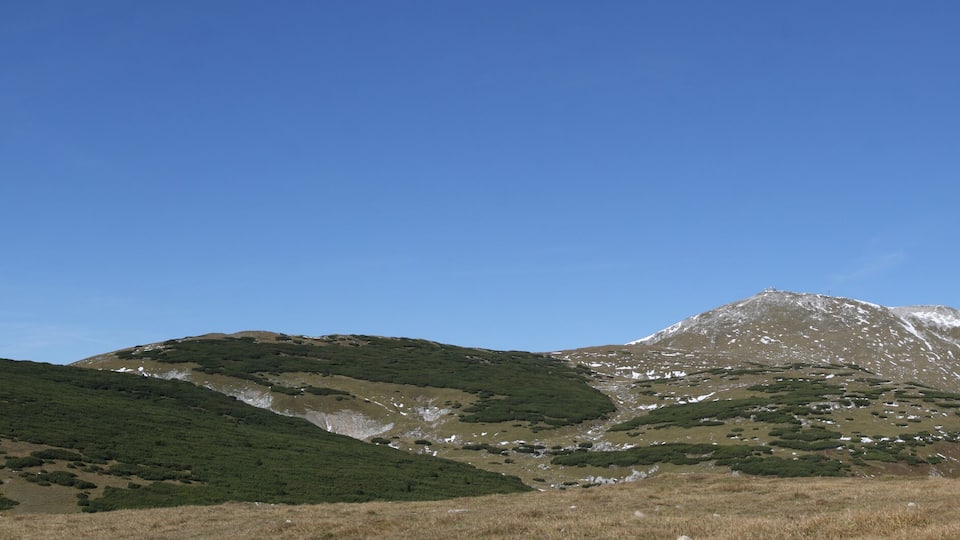 A mountain range with green vegetation and snow patches.