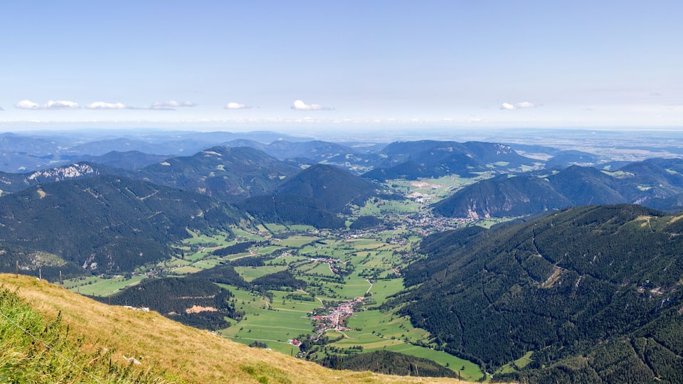 A mountainous landscape with a valley, green fields, and a small town.