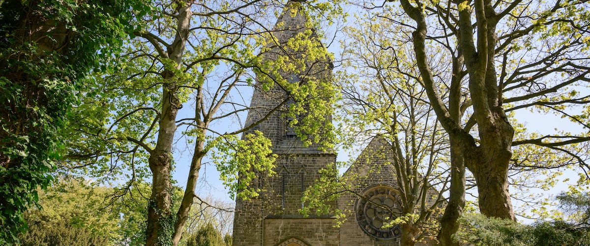 A historic church with a tall spire, surrounded by lush greenery and trees.