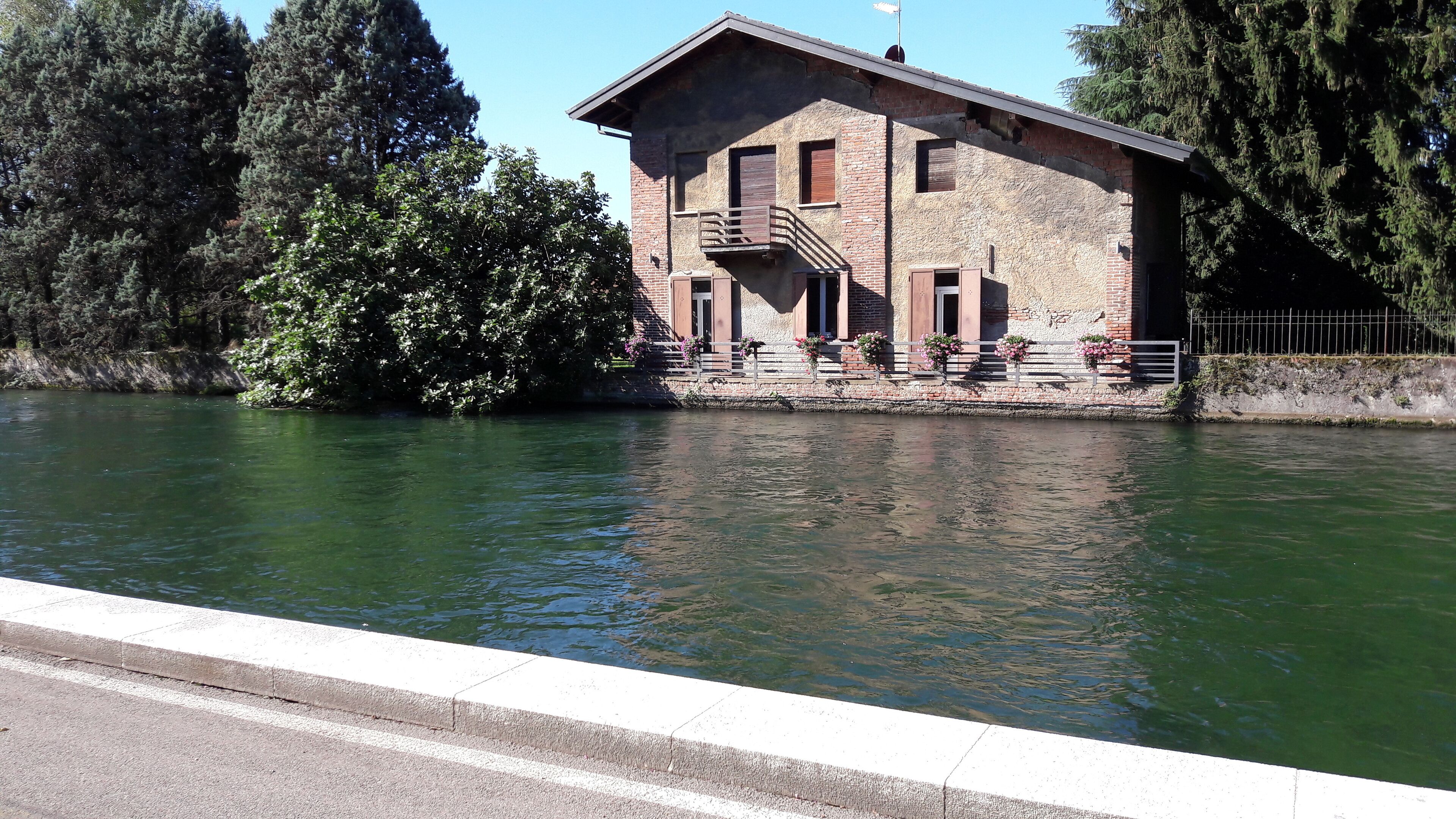 A riverside building with a balcony, surrounded by trees and a metal railing.