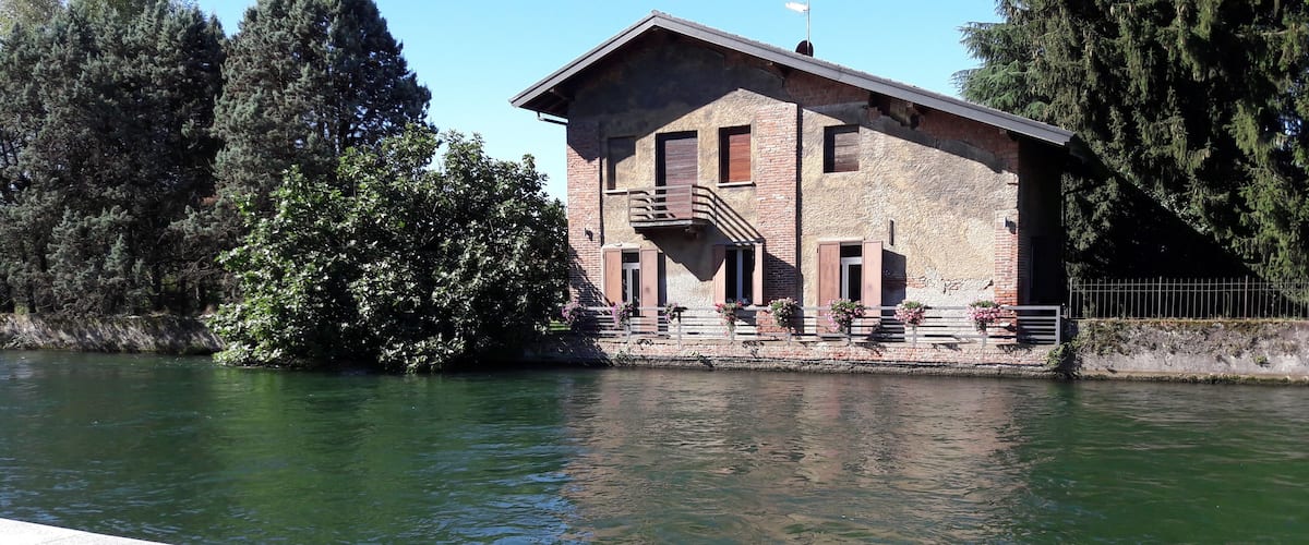 A riverside building with a balcony, surrounded by trees and a metal railing.
