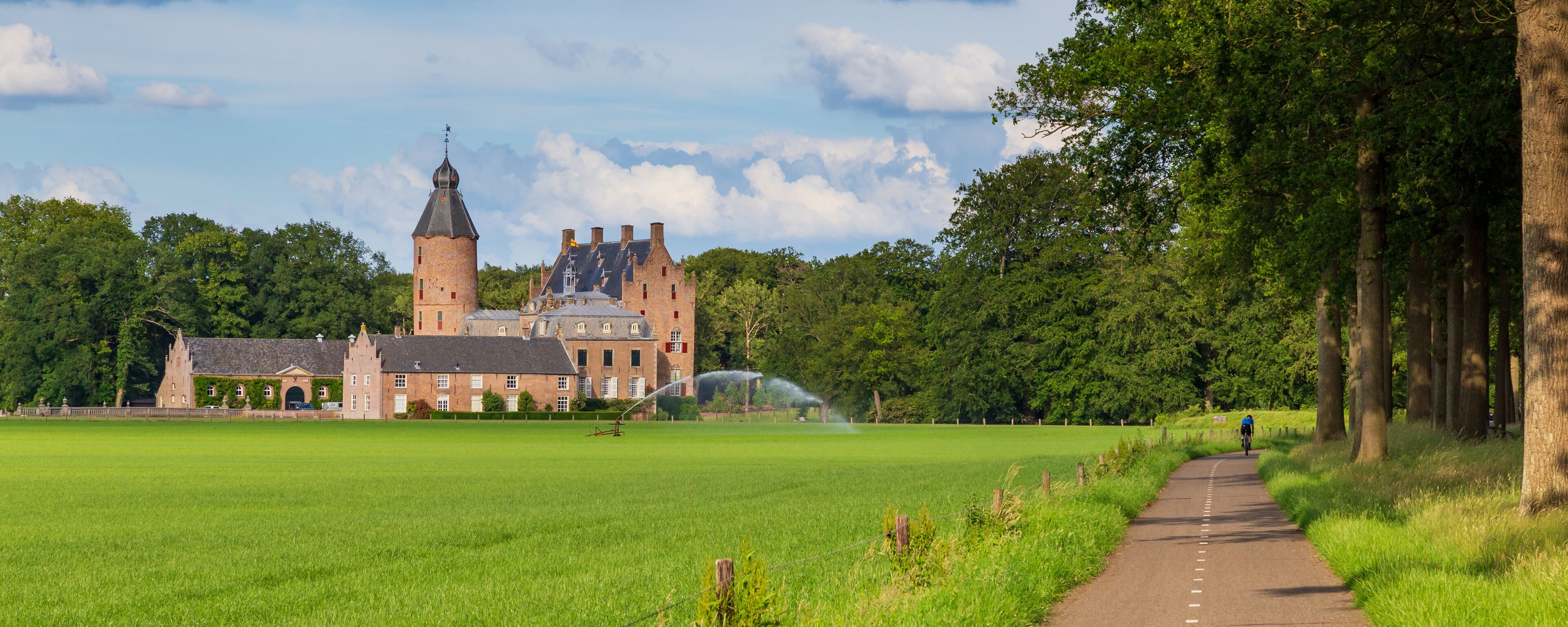 A historic castle with a tower, surrounded by a lush green field and a pathway.