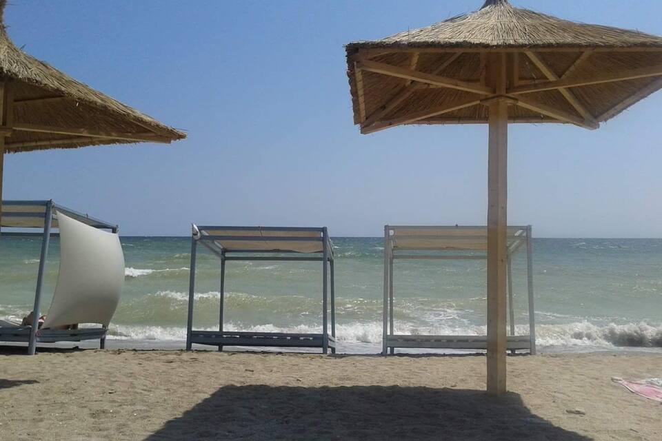 A beach with three empty sunbeds and two thatched umbrellas.