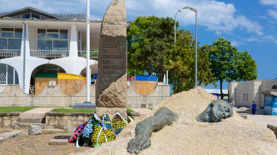 A monument with a plaque, a pile of sand, and colorful flowers in front of a building.