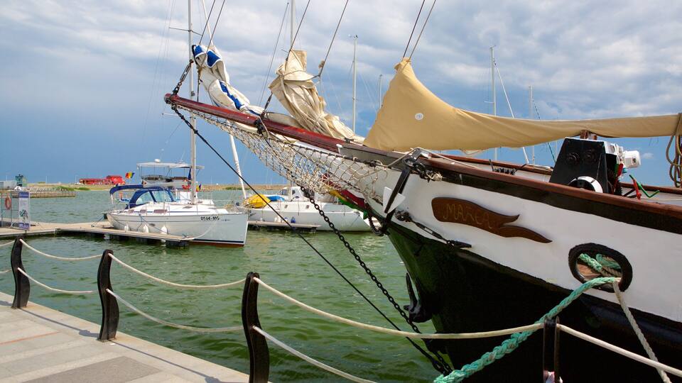 A marina with several sailboats docked, ropes securing the boats, and a clear sky.