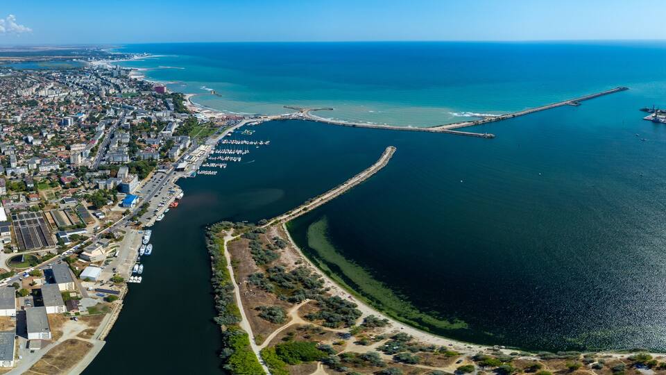 An aerial view of a coastal city with a marina, a long pier, and a large body of water.