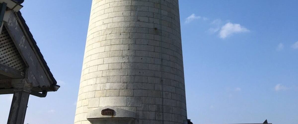 A tall, cylindrical tower with a dome on top, made of light-colored bricks, under a clear blue sky.